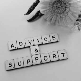 Advice & support Greyscale image of Scrabble tiles spelling 'Advice & Support' arranged on a surface, with a softly blurred background of flowers.