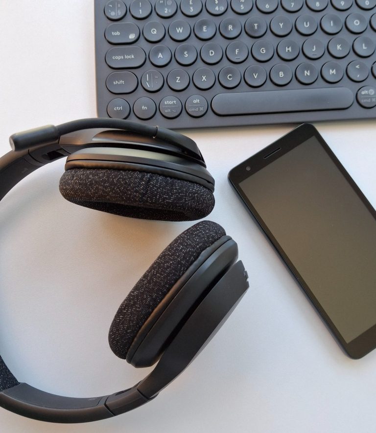A black keyboard with round keys, a black smartphone with a blank screen, and black over-ear headphones with fabric-covered ear pads.